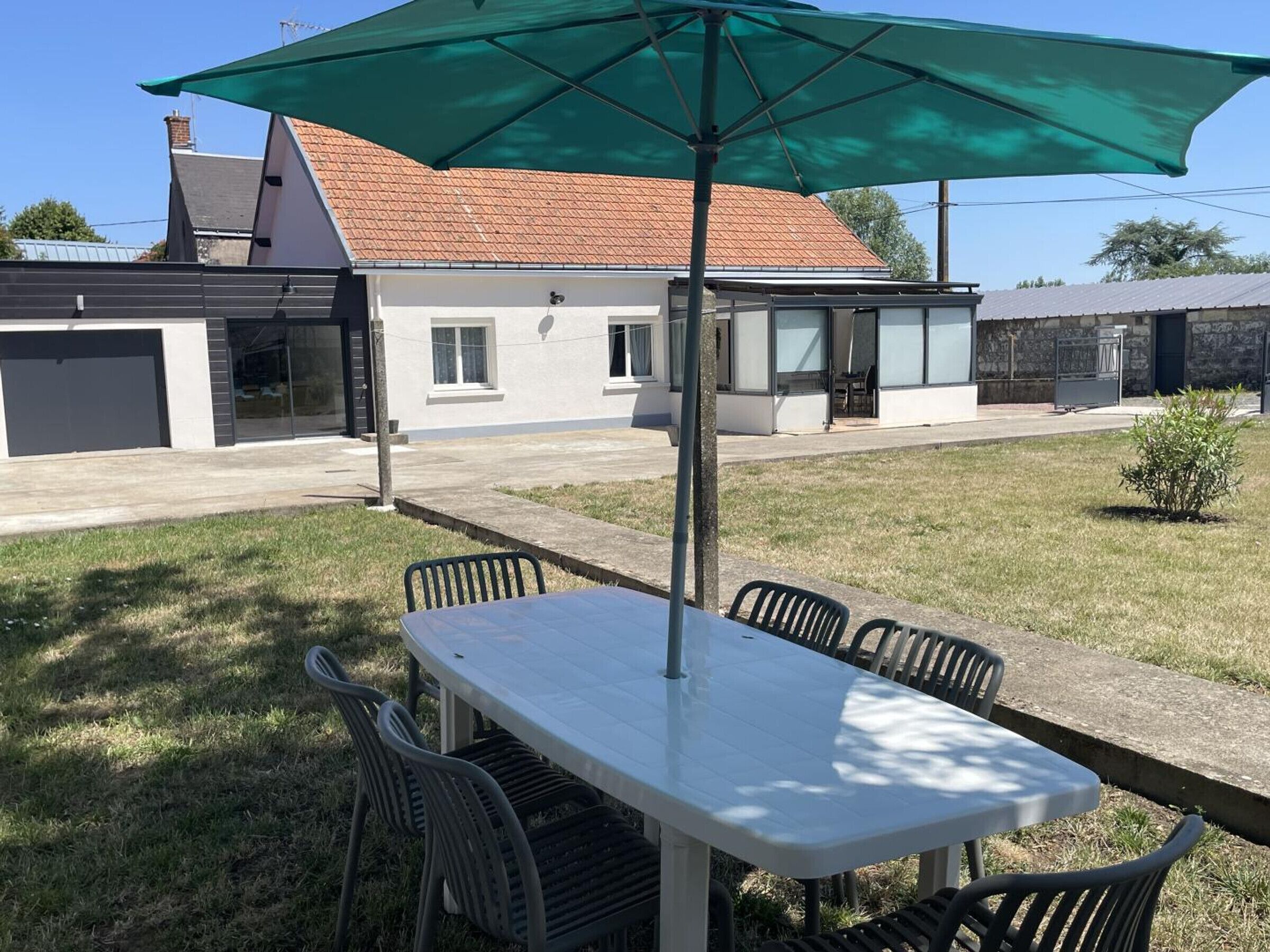 A patio with a table and chairs, a green umbrella, and a house with a tiled roof in the background.