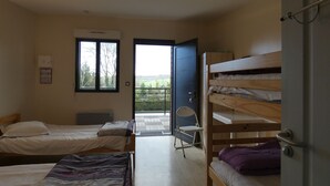 Et sovesal med to enkeltsenge, en køjeseng, en stol og en dør, der fører ud til en balkon.
