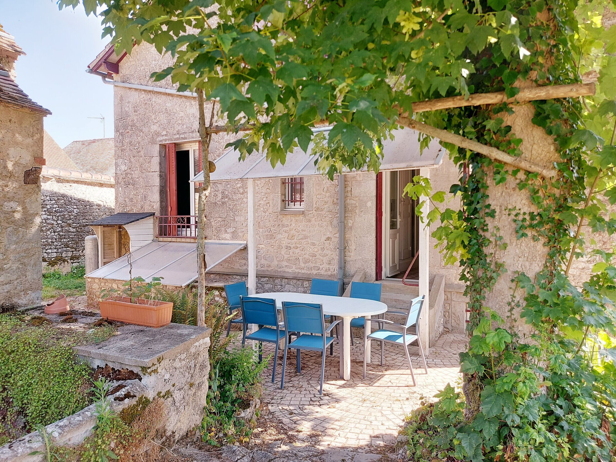 A stone building with a patio area featuring a table and chairs, surrounded by greenery and a stone wall.