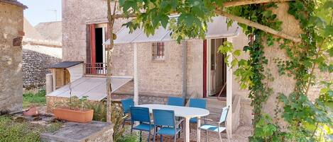 A stone building with a patio area featuring a table and chairs, surrounded by greenery and a stone wall.