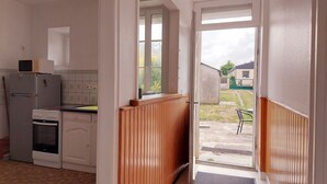 Een smalle gang met houten lambrisering, die uitkomt op een achtertuin.