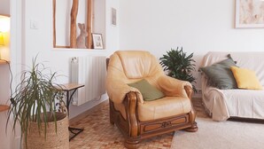Een woonkamer met een leren fauteuil, een tafeltje met een plant, een radiator en een bank met kussens.