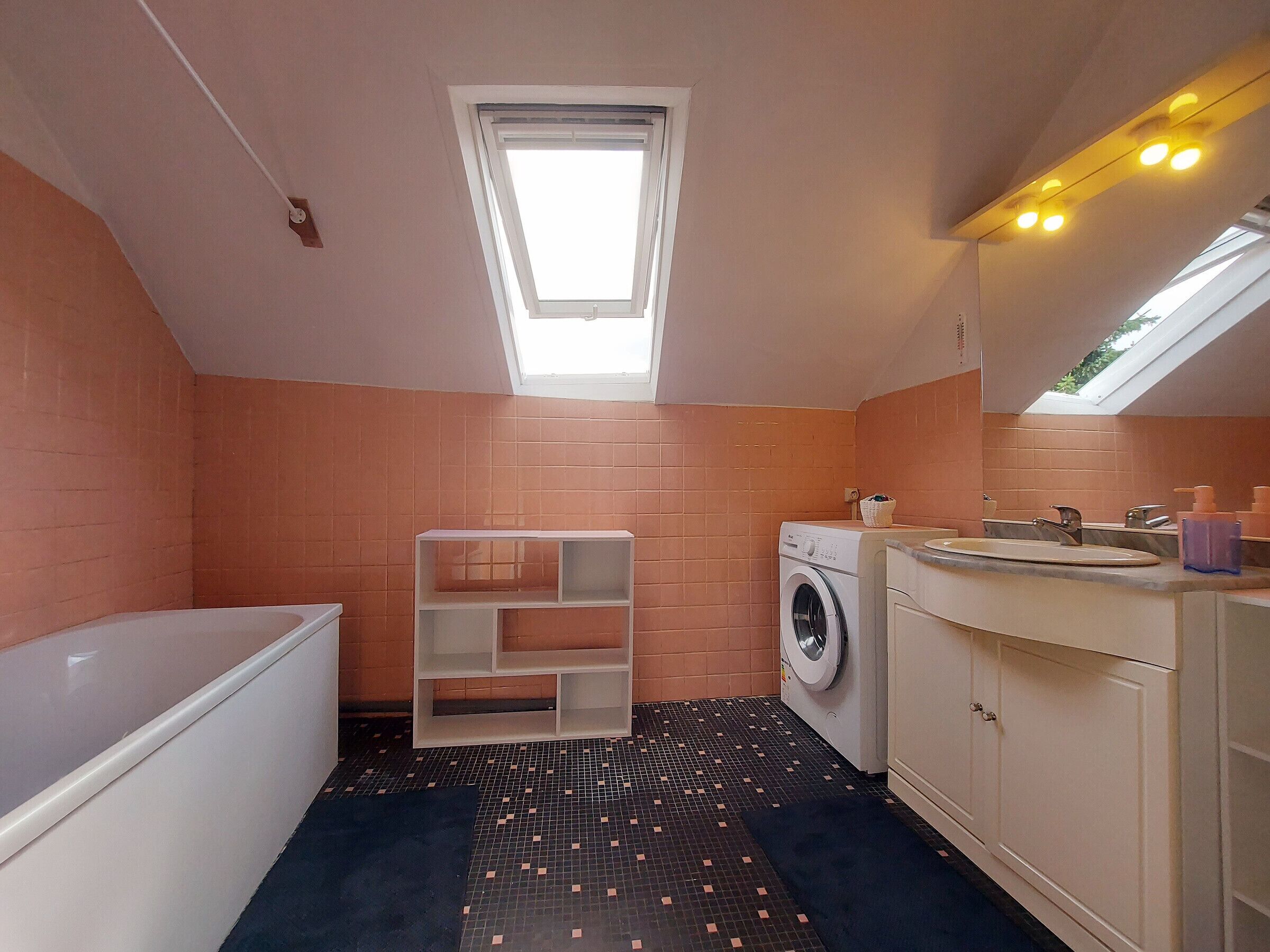 A compact bathroom with a skylight, a washing machine, a bathtub, and a sink with a mirror.