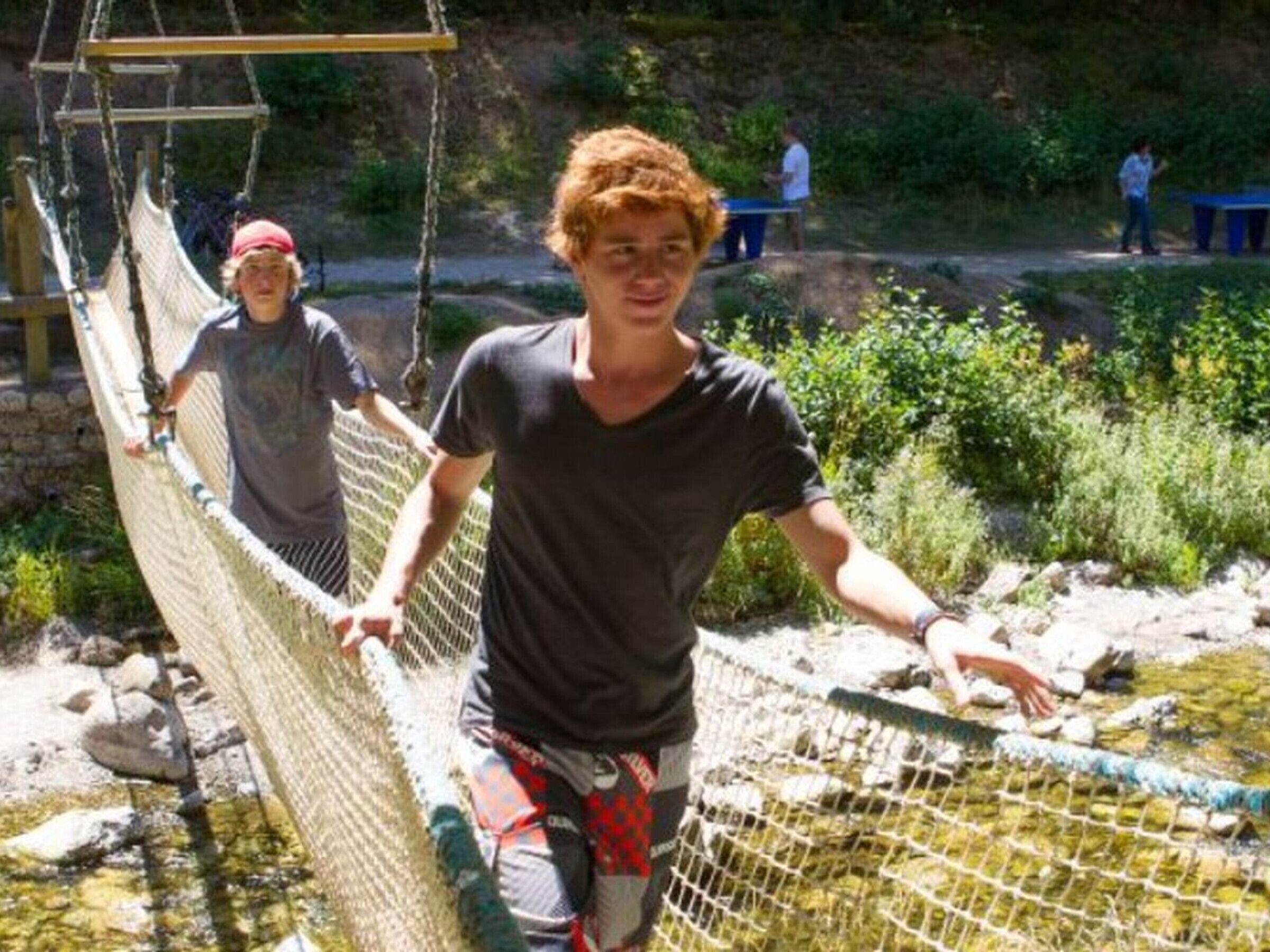 A rope bridge over a shallow stream with people on it.