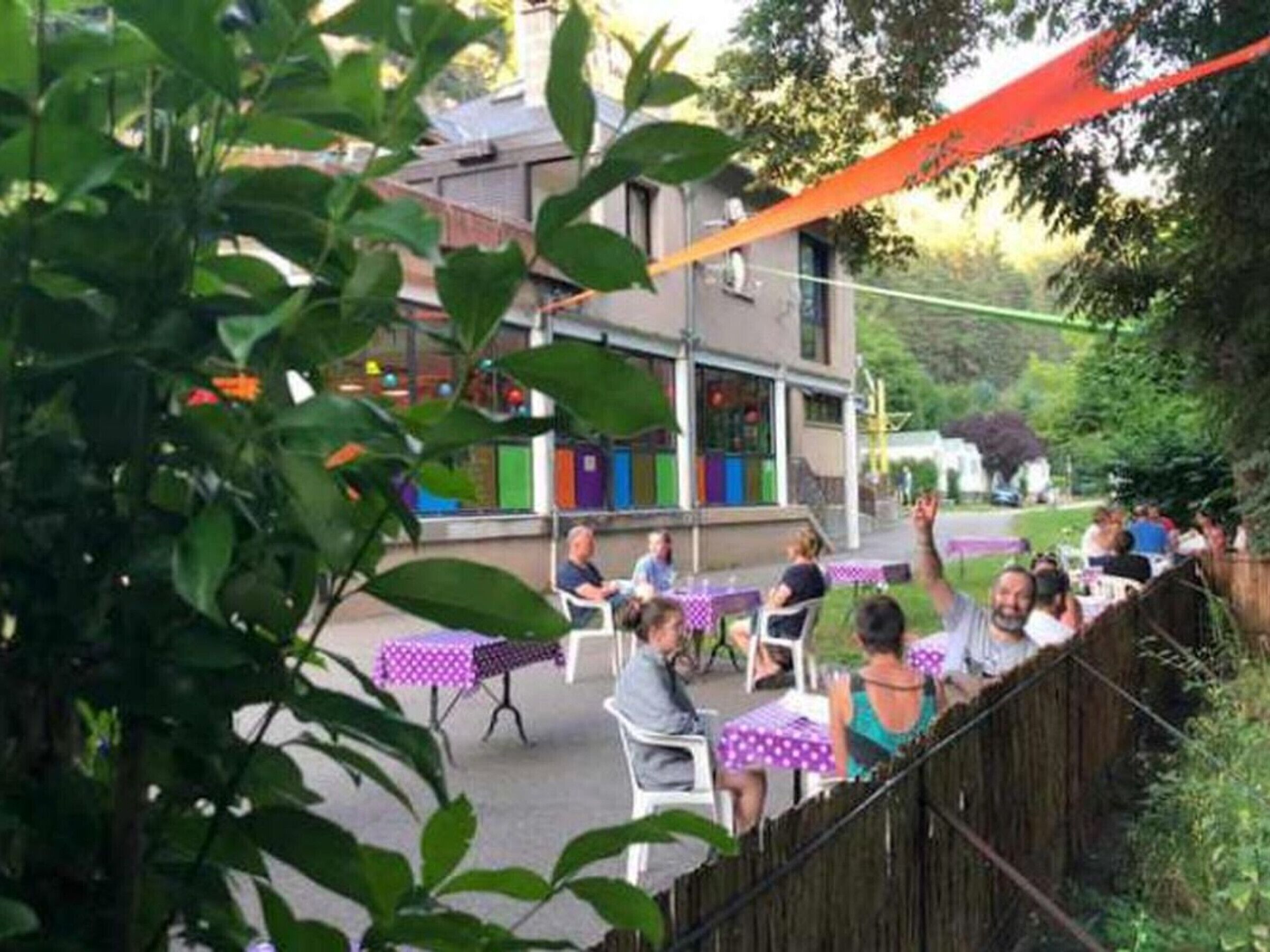 Un'area patio esterna con tavoli e sedie, un recinto in legno e un edificio sullo sfondo.