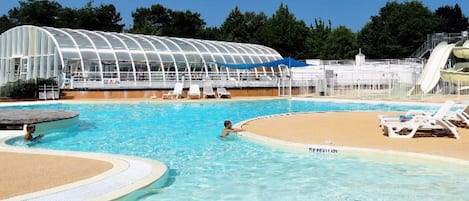 A swimming pool with a sandy area and lounge chairs, a covered structure, and a water slide.