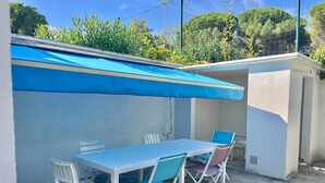 Une terrasse avec une table et des chaises, un auvent bleu et une vue sur la verdure.