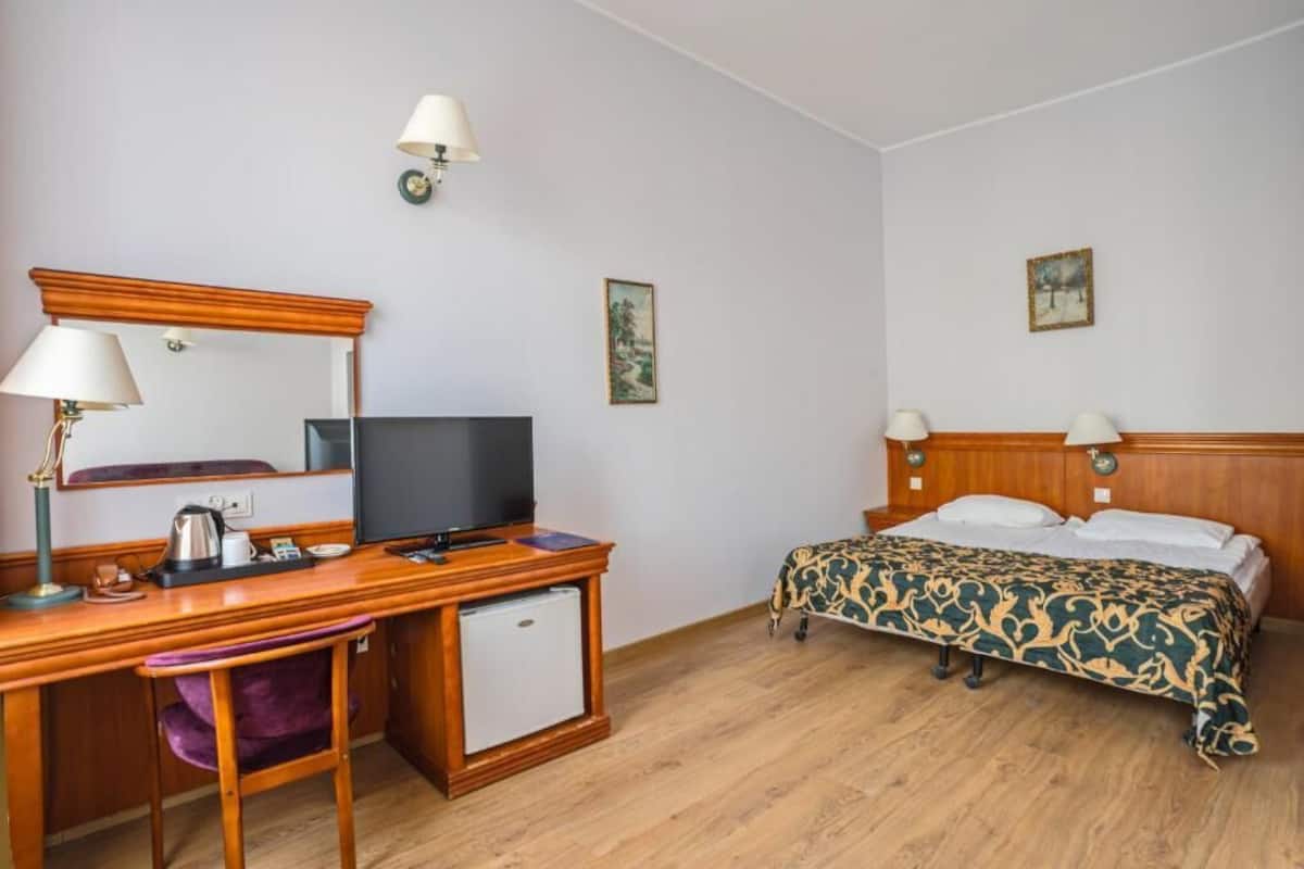Une chambre d’hôtel avec un bureau en bois, une télévision, un lit avec une literie à motifs et deux lampes fixées au mur.