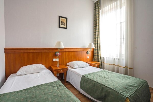 A hotel room with two single beds, wooden headboards, bedside tables with lamps, a framed picture on the wall, and a window with curtains. - Hotel Pietrak (Gniezno)