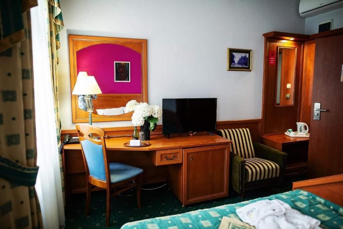Une chambre d’hôtel avec un bureau en bois, une télévision, une chaise, un lit et une armoire.