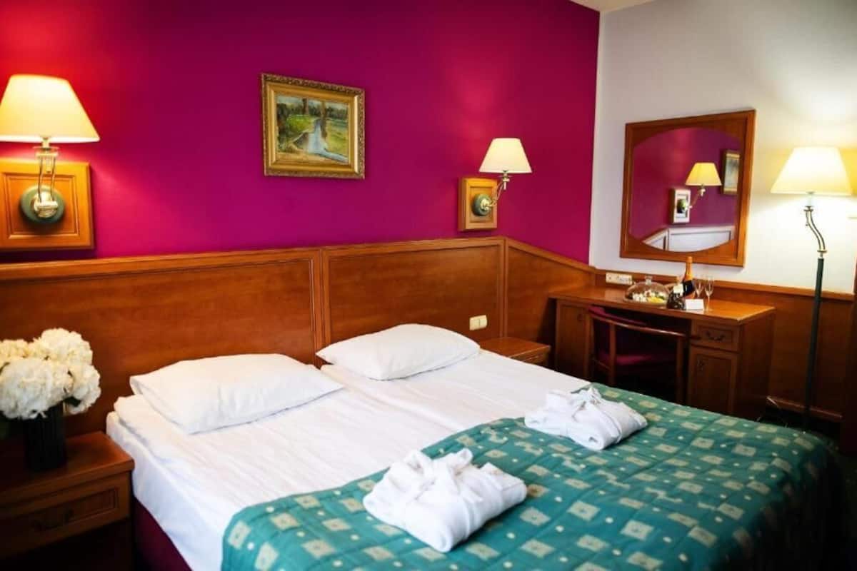 Une chambre d’hôtel avec deux lits, une tête de lit en bois, un bureau avec un miroir et deux lampes fixées au mur.