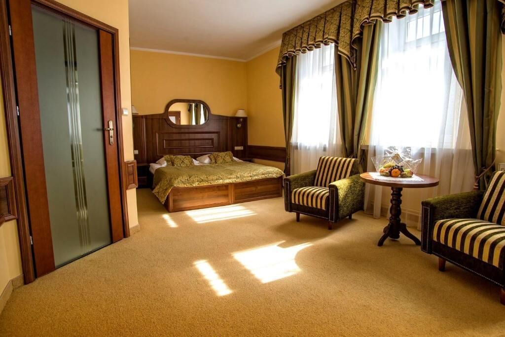 A hotel room with a bed, two armchairs, a round table with a vase, and a mirror on the wall.