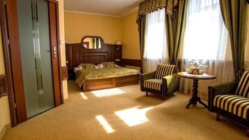 A hotel room with a bed, two armchairs, a round table with a vase, and a mirror on the wall.