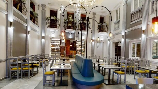 A spacious restaurant with high ceilings, chandeliers, and a central seating area with a blue cushioned bench.