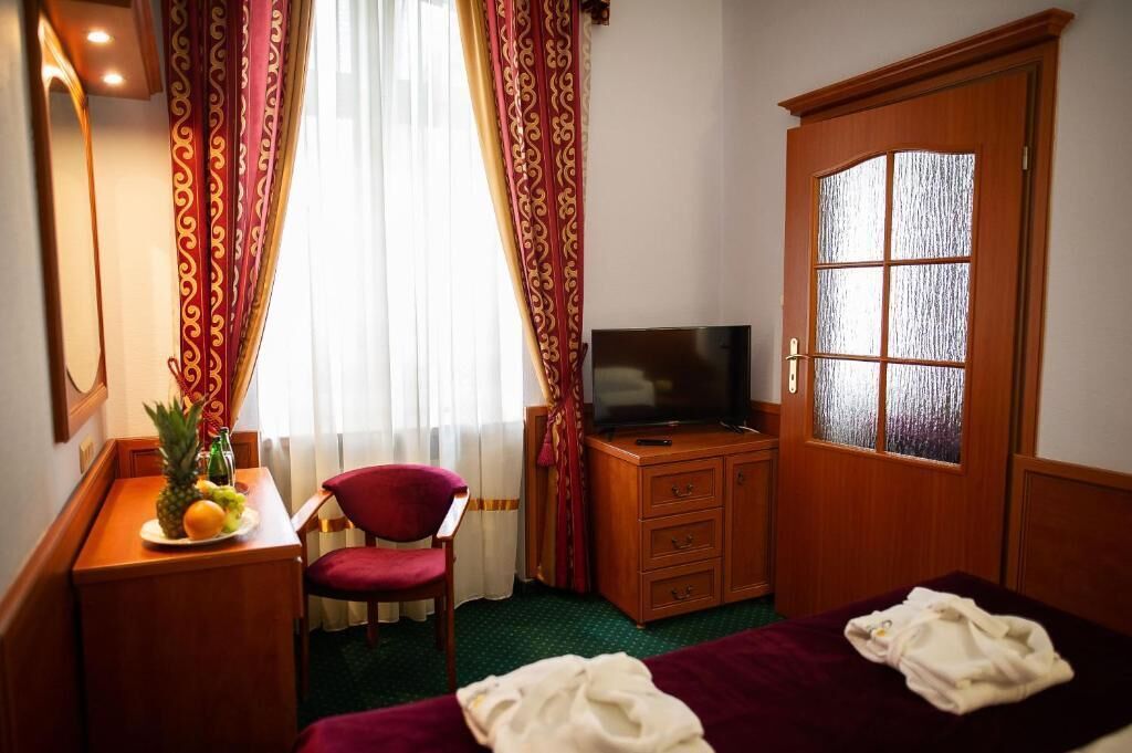 A hotel room with a bed, a television, a desk with a fruit bowl, a chair, and a wardrobe.