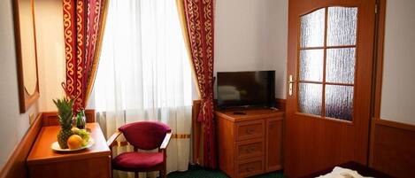 A hotel room with a bed, a television, a desk with a fruit bowl, a chair, and a wardrobe.