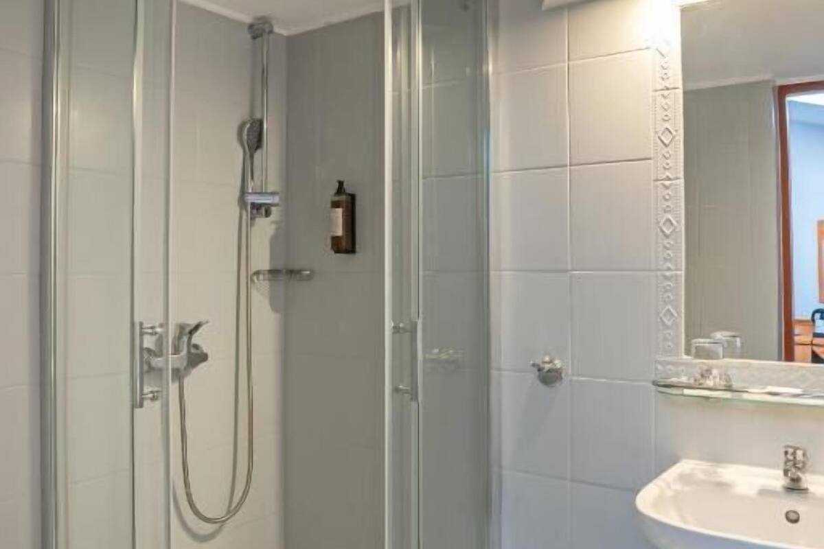 Une salle de bain moderne avec une douche à parois de verre, un lavabo blanc et un miroir orné d’une bordure de carreaux décoratifs.