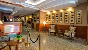 A hotel lobby with a reception desk, seating area, framed photographs on the wall, and a chandelier.