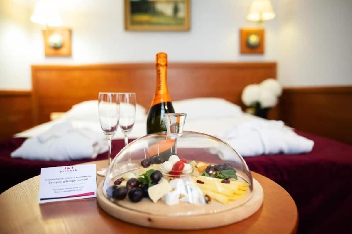 Une chambre d’hôtel avec un lit, une table de chevet sur laquelle se trouve une bouteille de champagne, des verres et une assiette de fromages sur une table.