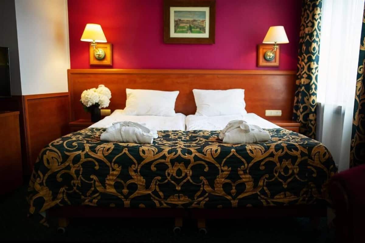 Un lit double avec une couvre-lit à motifs, deux lampes de chevet, une horloge et un tableau encadré au mur.