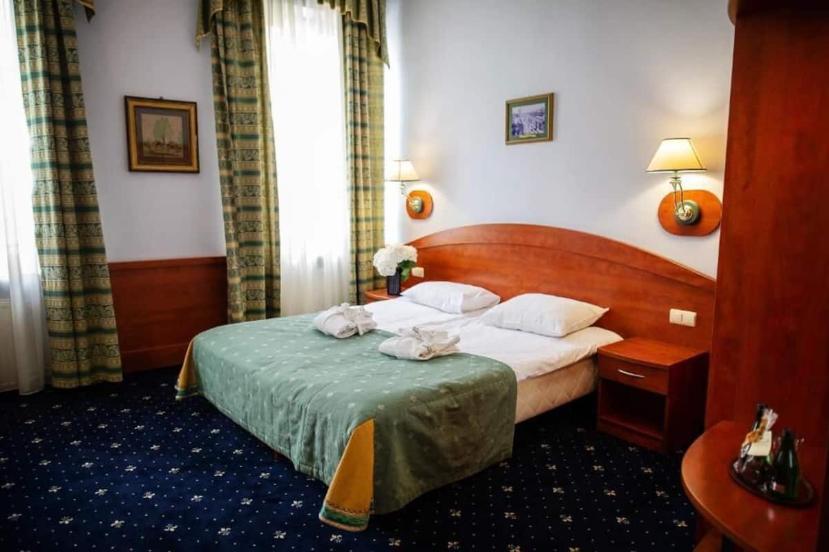 Une chambre d’hôtel avec un lit simple, deux tables de chevet, une tête de lit en bois et deux lampes fixées au mur.