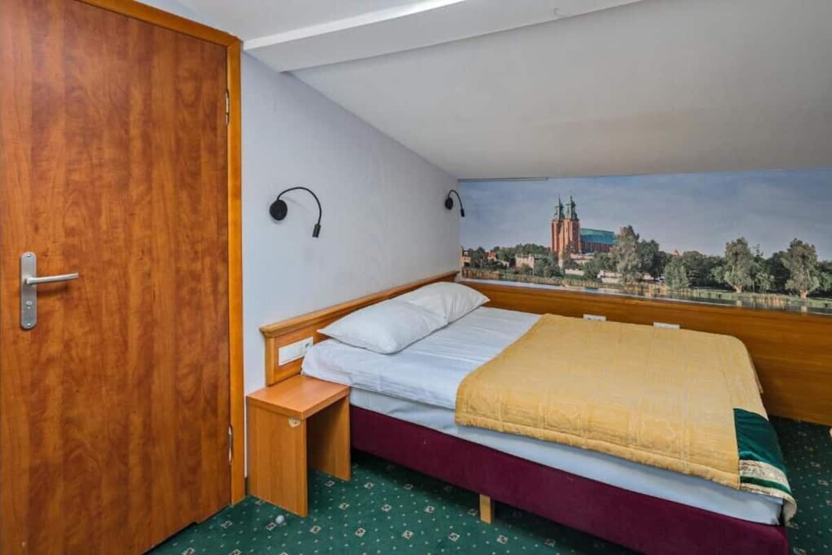 Une chambre à coucher avec un lit, une table de chevet, une porte en bois et une fresque représentant un paysage urbain sur le mur.