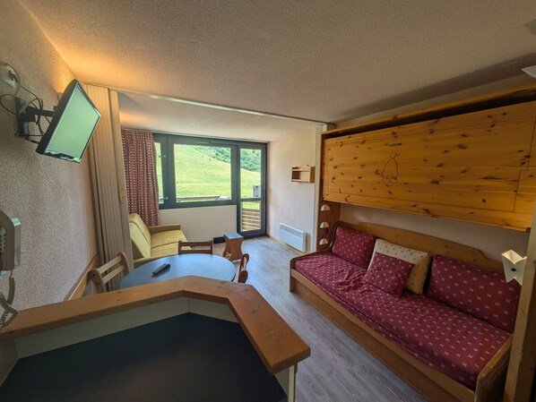 Una habitación acogedora con un sofá de madera, una mesita y un televisor montado en la pared.