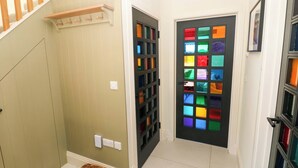 Un pasillo con una escalera de madera, una puerta con paneles de vidrio emplomado de colores, y una cesta en el suelo.
