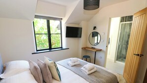 Un dormitorio con cama, escritorio, espejo y ducha.