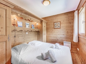Um quarto de madeira com uma cama, uma estante de livros e uma pequena janela.