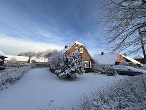 A residential area with houses, a snow-covered lawn, and a car parked in the driveway. - Detached vacation home in Nessmersiel (near Deich): own garden & wallbox (Dornum)