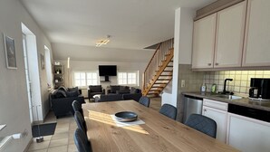 Una cucina moderna con un tavolo da pranzo in legno, sedie nere e una scala che conduce a una zona mansardata.