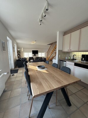 A modern kitchen with a wooden dining table, black chairs, and a staircase leading to a loft. - Detached vacation home in Nessmersiel (near Deich): own garden & wallbox (Dornum)