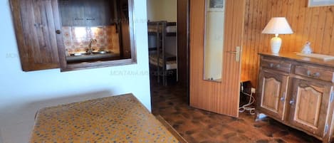 Une pièce comprenant un lit, une armoire en bois, une petite fenêtre et une porte donnant sur une autre pièce.