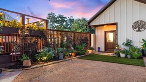 A well-maintained garden with a gravel path leading to a building with a wooden door and a tree decoration on the wall. - Secret Garden Cottage - Walk to Main St. (Fredericksburg)