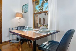 A dining area with a wooden table, black chairs, a lamp, and a window with a view of trees. - Secret Garden Cottage - Walk to Main St. (Fredericksburg)