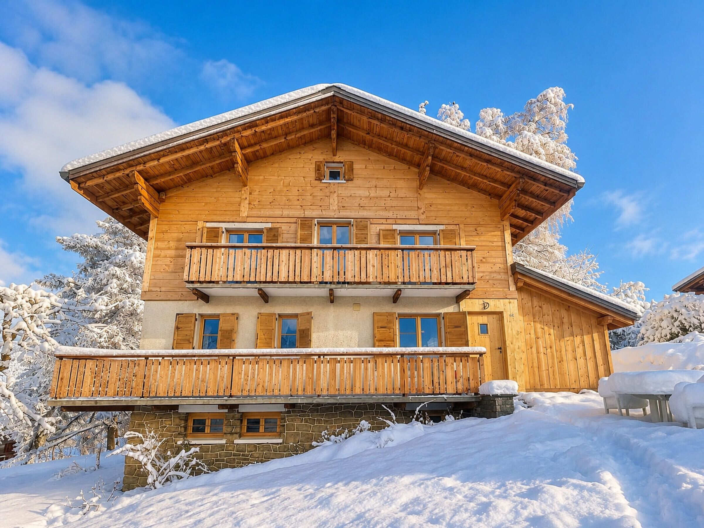Un chalet de madera de varios pisos con un balcón en el segundo nivel, rodeado de árboles cubiertos de nieve.