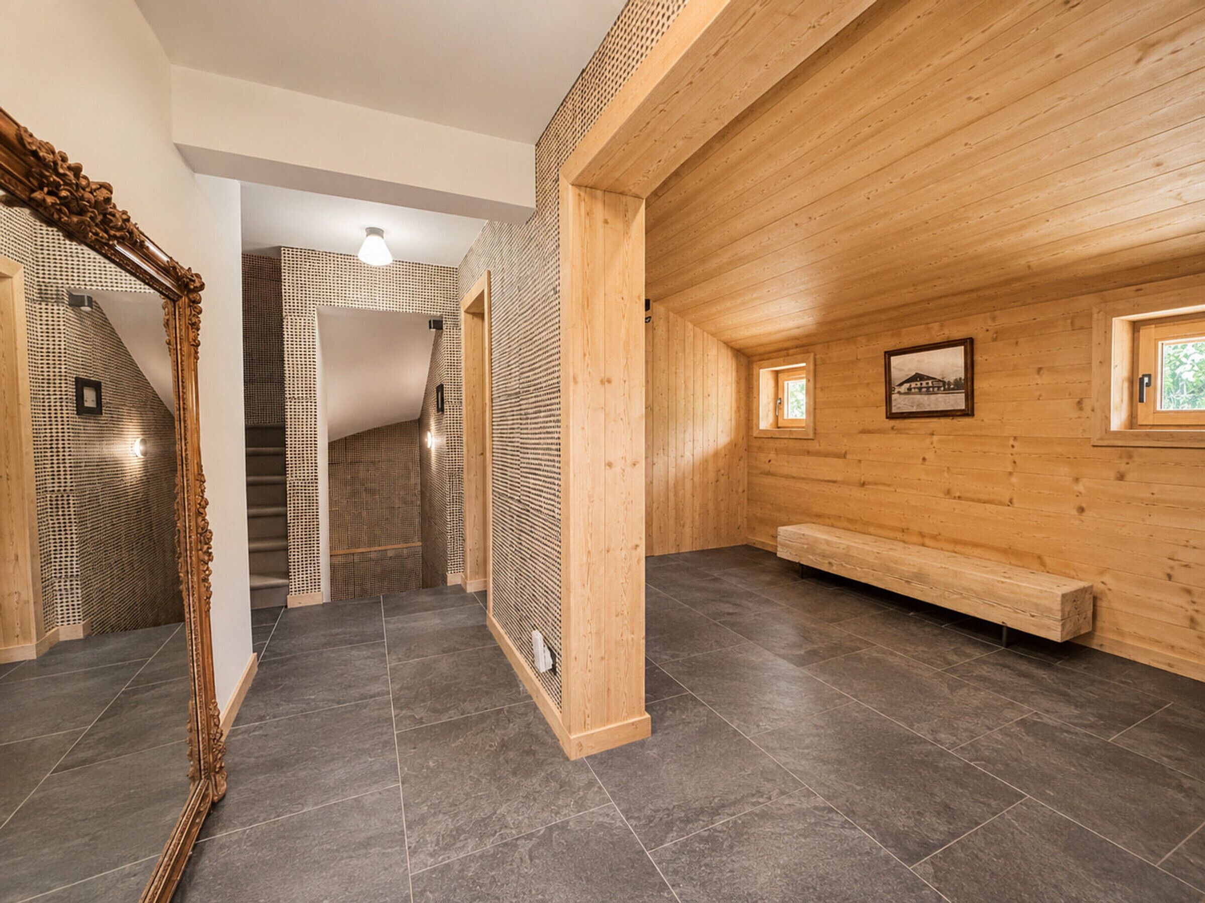 Un interior moderno con un banco de madera, un espejo grande y una escalera.