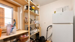 Une cuisine de taille réduite, avec des étagères en bois, un réfrigérateur et un aspirateur.