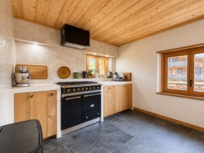 A kitchen with a stove, cabinets, and a window overlooking a wooden structure.
