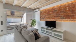 A modern living room with a sofa, TV, and a brick accent wall. - Holiday Home 'El Racó Del Mas' with Private Terrace, Wi-Fi & Air Conditioning (Canet de Mar)