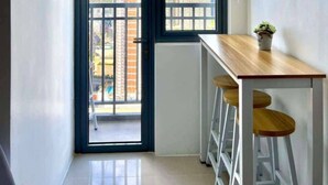 Una cocina moderna con aire acondicionado integrado, una ventana con vistas a edificios altos y un pequeño comedor con taburetes.