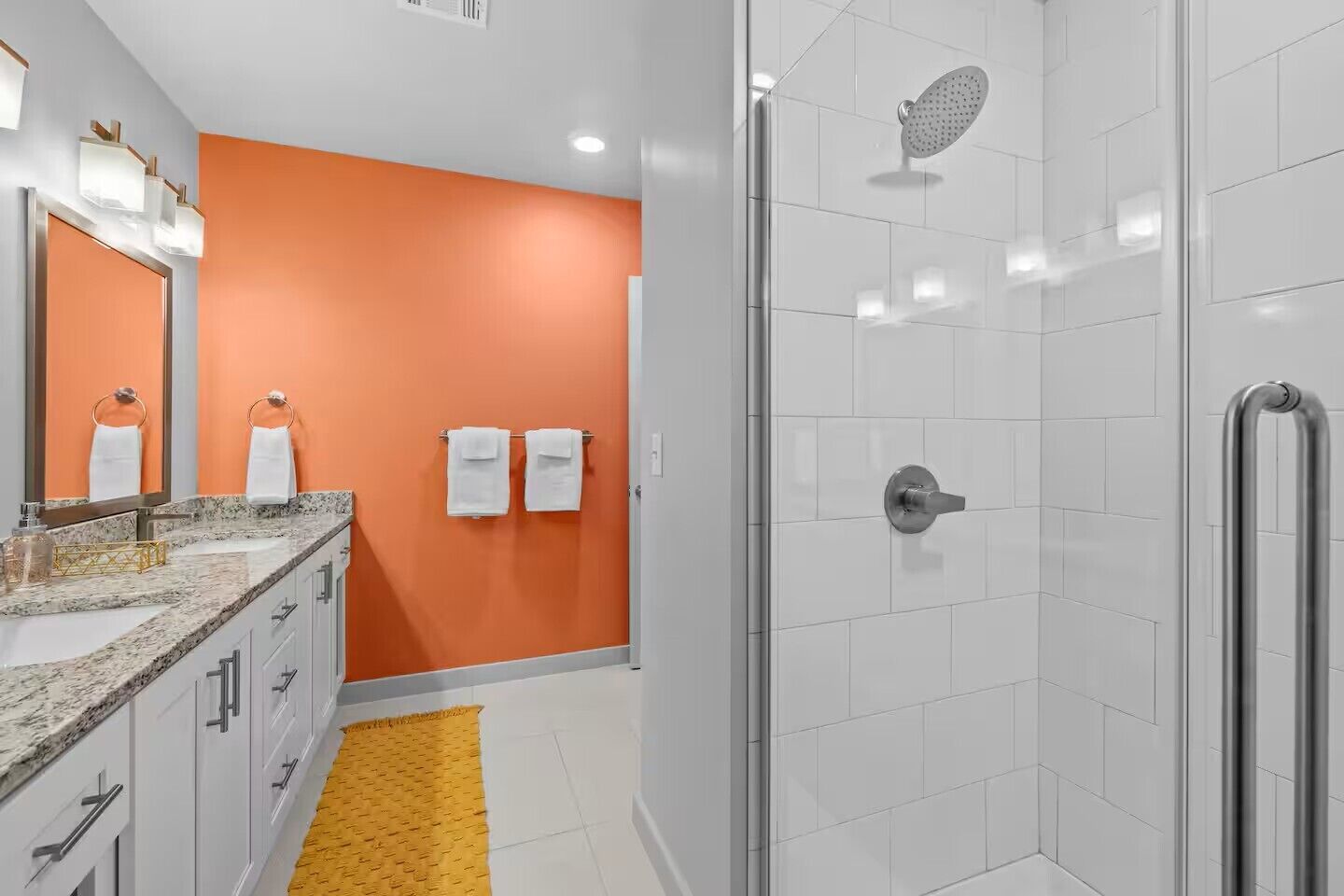 A modern bathroom with a shower, a vanity with a granite countertop, and a yellow rug.