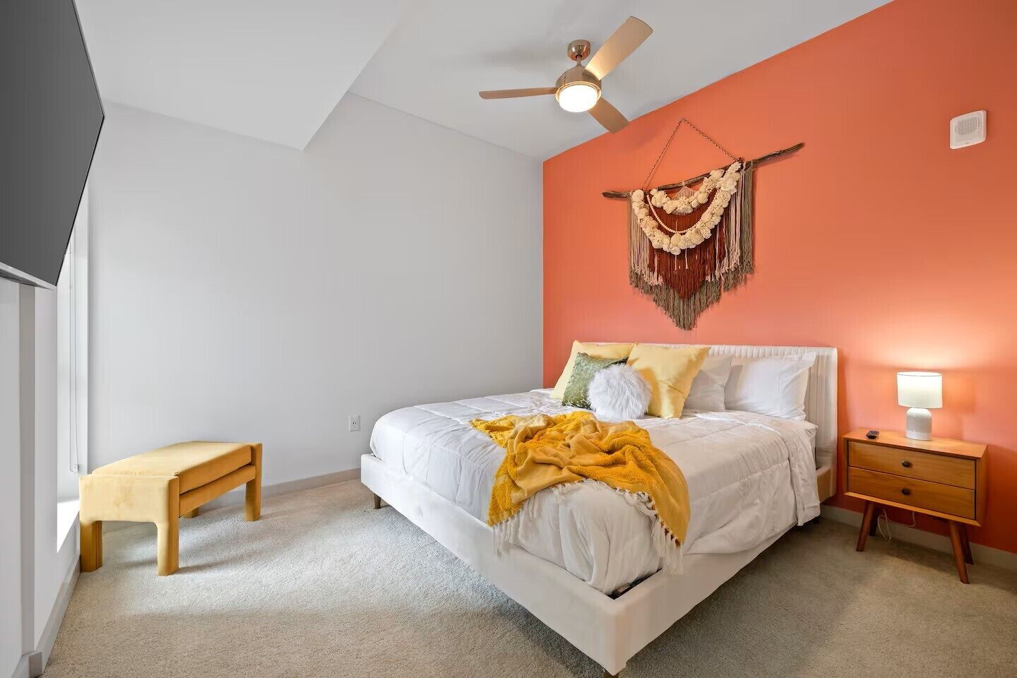 Ein Schlafzimmer mit einem Bett, einem Nachttisch, einer Bank, einem Deckenventilator und einer Wanddekoration aus Makramee.