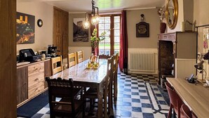 A dining area with a checkered floor, wooden table, chairs, and a kitchen area with appliances. - Gîte Montana 3 pers. plein center Mirepoix - Terrace, garden, barbecue (Mirepoix)