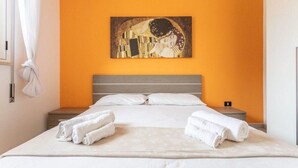 A hotel room with a bed, white towels, an orange wall, and a painting above the bed. - Tulip house with sea view in Torre Vado (Torre Vado)