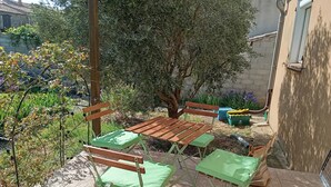An outdoor patio with a wooden table and green chairs, surrounded by plants and a tree. - At Lia and Danny's (Rieux-Minervois)