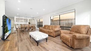 A spacious living room with a large flat-screen TV, a brown leather sofa, a matching armchair, and a patterned ottoman. - Happy Cozy Convenient 4BR, Breezy, Near Mall, Park (Berwick)