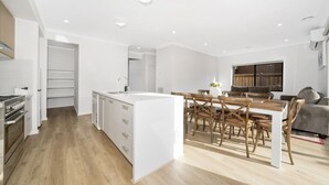 A modern kitchen with white cabinetry, a central island, and a dining area with wooden chairs and a table. - `Brand New`, Spacious, Breezy Comfy, Luxury Home ! (Berwick)