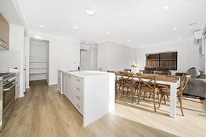 A modern kitchen with white cabinetry, a central island, and a dining area with wooden chairs and a table. - `Brand New`, Spacious, Breezy Comfy, Luxury Home ! (Berwick)